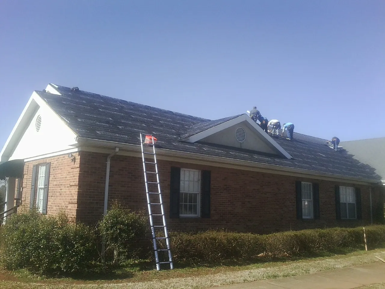 Crew tearing shingles off a brick ranch roof with a ladder set — Metal Roof Repair work by our crew in Kunkletown