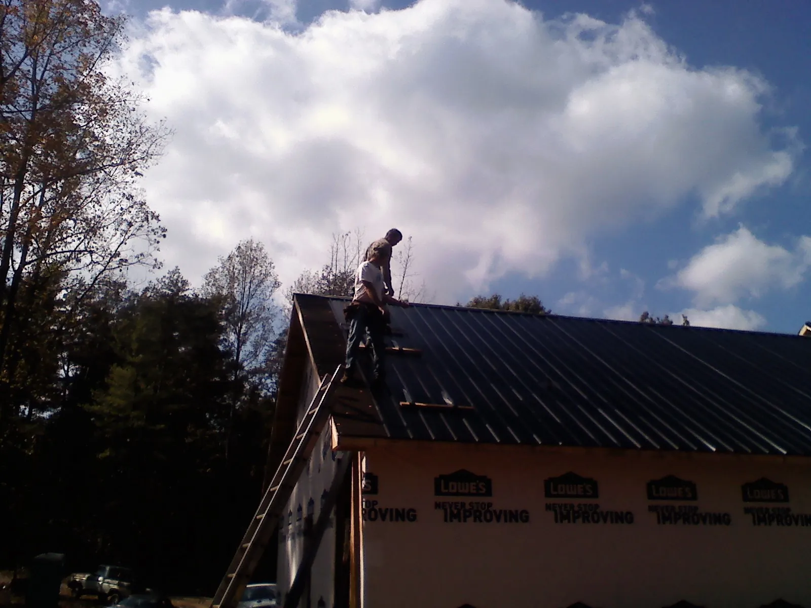 Roofer fastening dark metal panels high against a cloudy sky, from a Roof Inspection job in Kunkletown