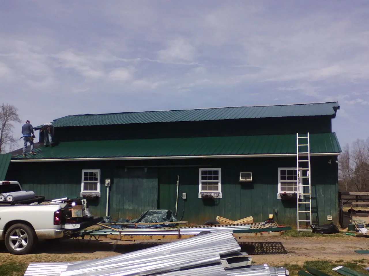 Crew installing green metal roofing on a large green barn in Kunkletown