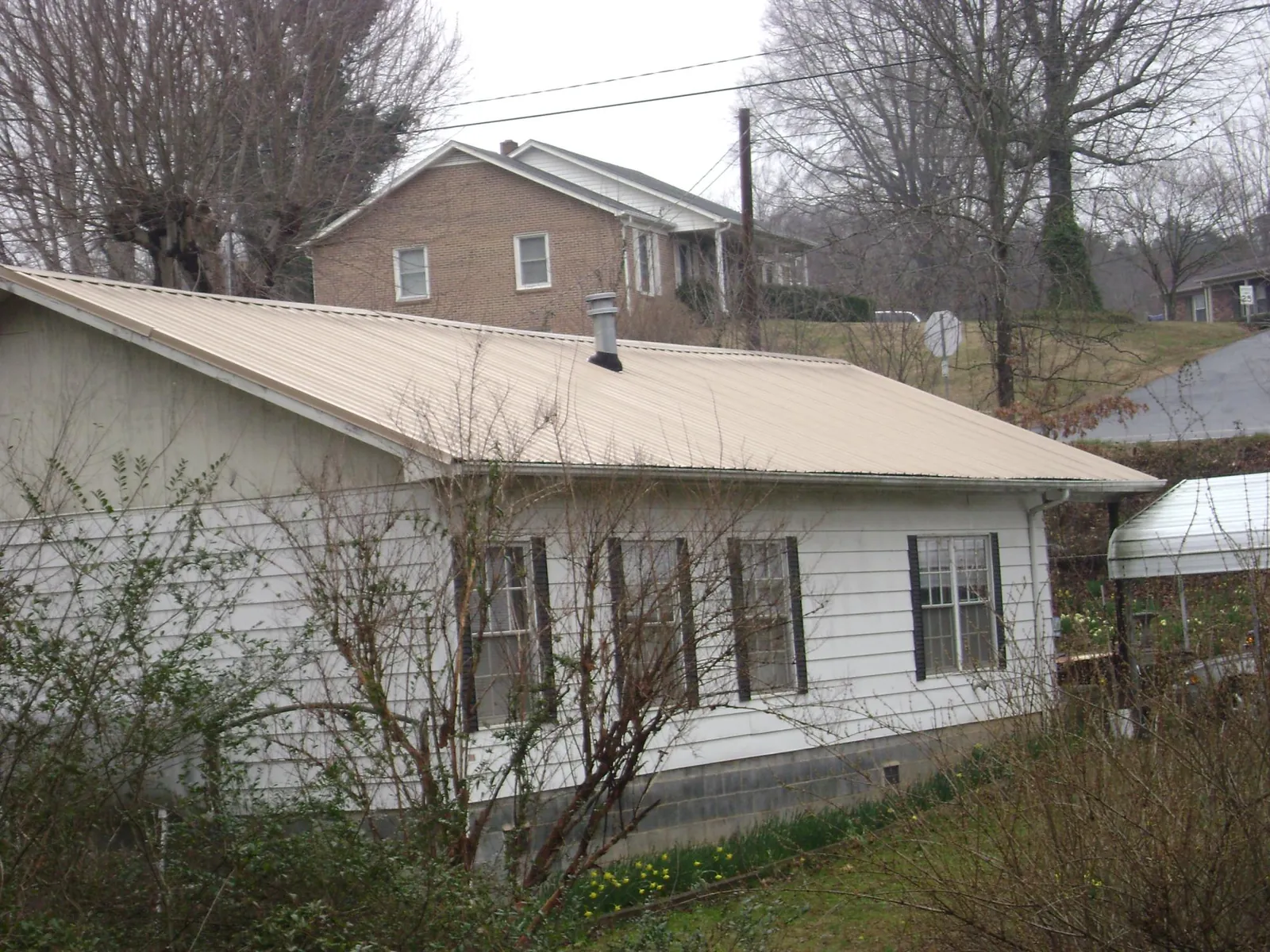 Tan metal roof on a white sided house set into a hillside — Commercial Roofing by Roofing Brothers in Kunkletown